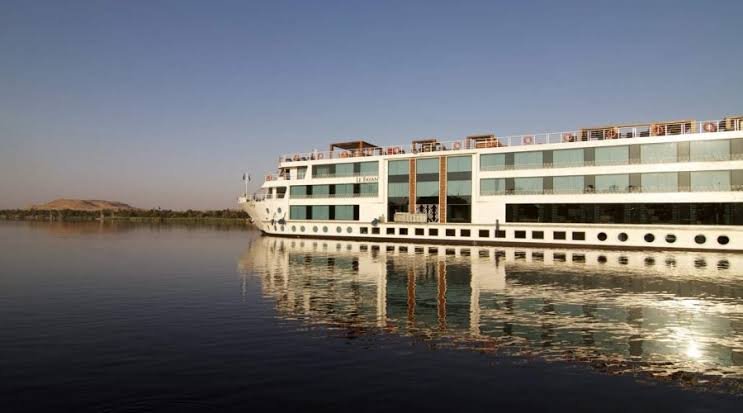 Barco de crucero por el Nilo navegando al atardecer, reflejado en el agua en calma