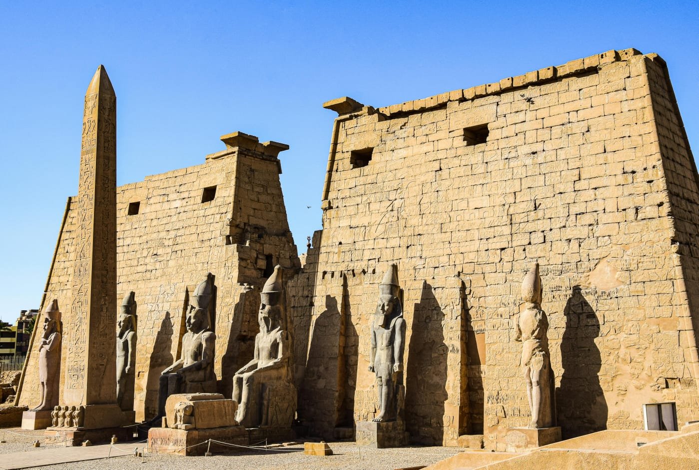 El primer pilono del templo de Luxor con el obelisco en pie, los colosos sentados de Ramsés II y las estatuas de pie a lo largo de la fachada, a plena luz del día.