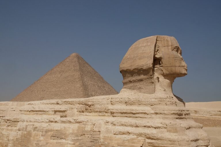 La Gran Esfinge de Giza de perfil junto a la Gran Piramide de Keops bajo un cielo azul intenso, dos iconos eternos del antiguo Egipto cerca de El Cairo