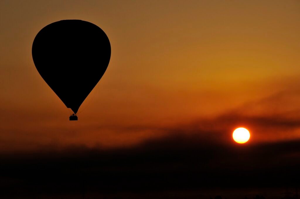 Globo aerostatico en silueta sobre un amanecer dorado en Luxor Egipto con el sol bajo en el horizonte junto al valle del Nilo