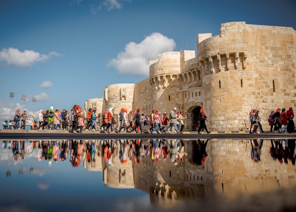 La Ciudadela de Qaitbay en Alejandria con su reflejo en el agua, muros de piedra dorada bajo un cielo azul y la corniche junto al Mediterraneo