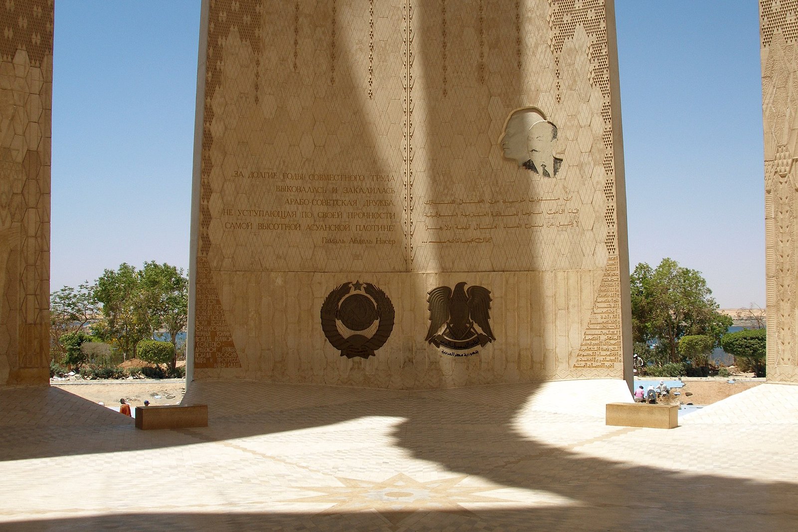 Monumento del loto de la Alta Presa de Asuan en Egipto, con emblemas grabados e inscripciones bajo el arco de piedra y vegetacion alrededor