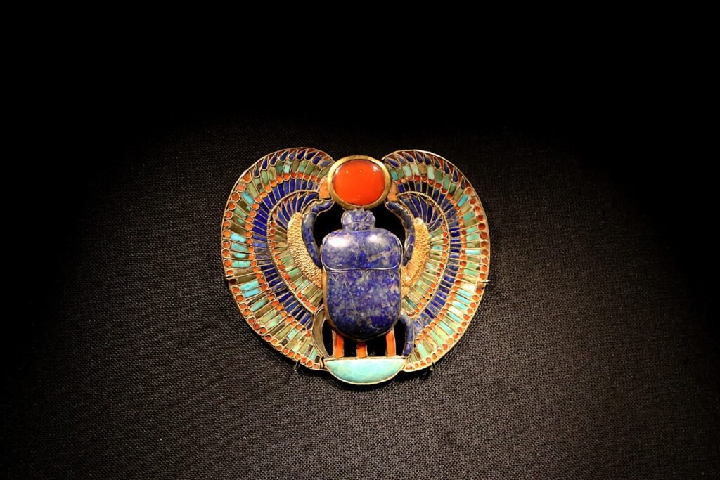 Pectoral egipcio con escarabajo de lapislazuli y alas de cloisonne multicolor y disco solar de cornalina, joyeria de oro antiguo sobre fondo oscuro