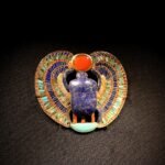 Pectoral egipcio con escarabajo de lapislazuli y alas de cloisonne multicolor y disco solar de cornalina, joyeria de oro antiguo sobre fondo oscuro