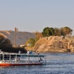 Barco turistico navegando el Nilo al atardecer en Asuan con dunas doradas, rocas de granito y palmeras junto a la isla Elefantina en Egipto
