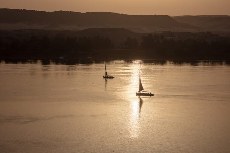Dos feluccas en silueta navegando el Nilo al atardecer con el reflejo dorado del sol sobre el agua y colinas del desierto al fondo en Egipto
