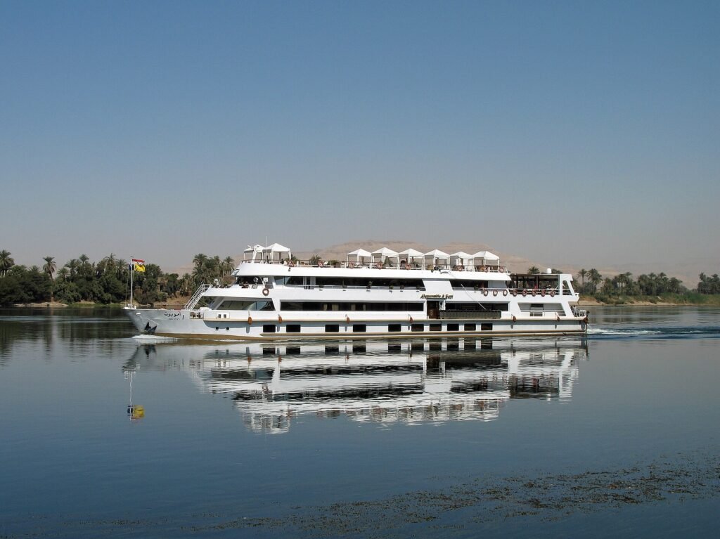 Barco de crucero blanco navegando por el rio Nilo en Egipto con cielo azul y palmeras en la orilla