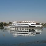 Barco de crucero blanco navegando por el rio Nilo en Egipto con cielo azul y palmeras en la orilla
