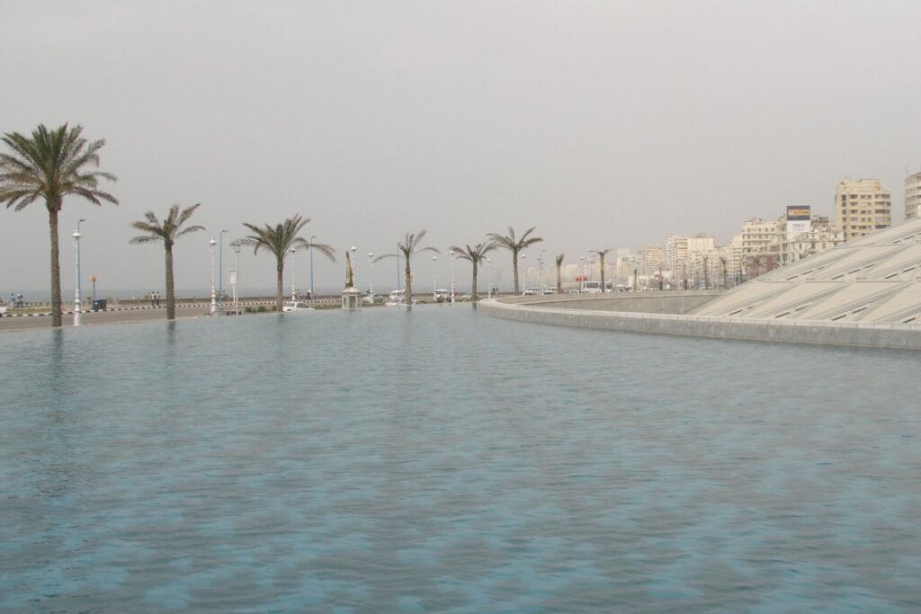 La emblematica Biblioteca de Alejandria con su techo en forma de disco inclinado junto al mar y palmeras de la corniche en Egipto