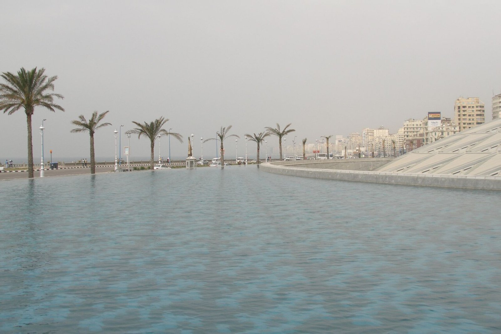 La emblematica Biblioteca de Alejandria con su techo en forma de disco inclinado junto al mar y palmeras de la corniche en Egipto