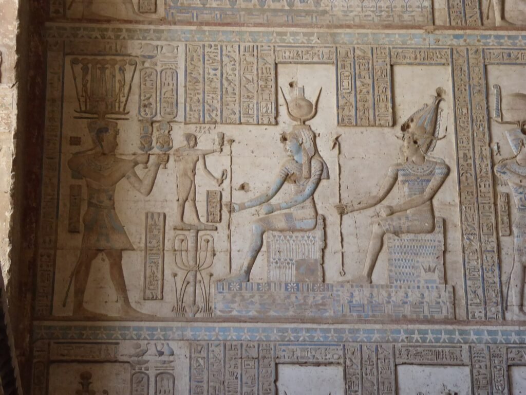 Relieve policromado en el templo de Dendera con figuras ptolemaicas sentadas tipo Cleopatra y Cesarion, pintura azul y ocre conservada y jeroglificos nitidos en piedra clara
