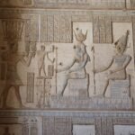 Relieve policromado en el templo de Dendera con figuras ptolemaicas sentadas tipo Cleopatra y Cesarion, pintura azul y ocre conservada y jeroglificos nitidos en piedra clara