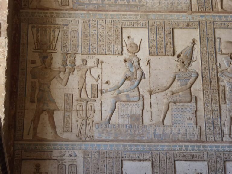 Relieve policromado en el templo de Dendera con figuras ptolemaicas sentadas tipo Cleopatra y Cesarion, pintura azul y ocre conservada y jeroglificos nitidos en piedra clara