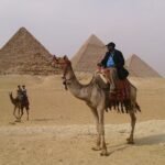 Hombre montado en un camello frente a las piramides de Guiza en Egipto para planificar un viaje a Egipto