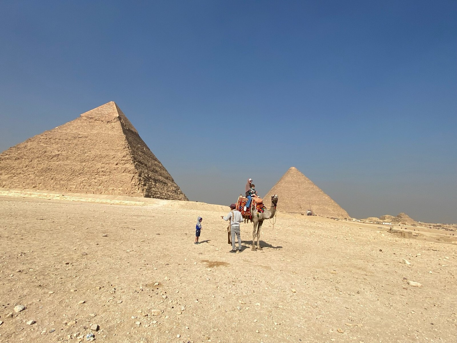 Camello con jinetes y turistas ante las piramides de Guiza bajo cielo azul en Egipto