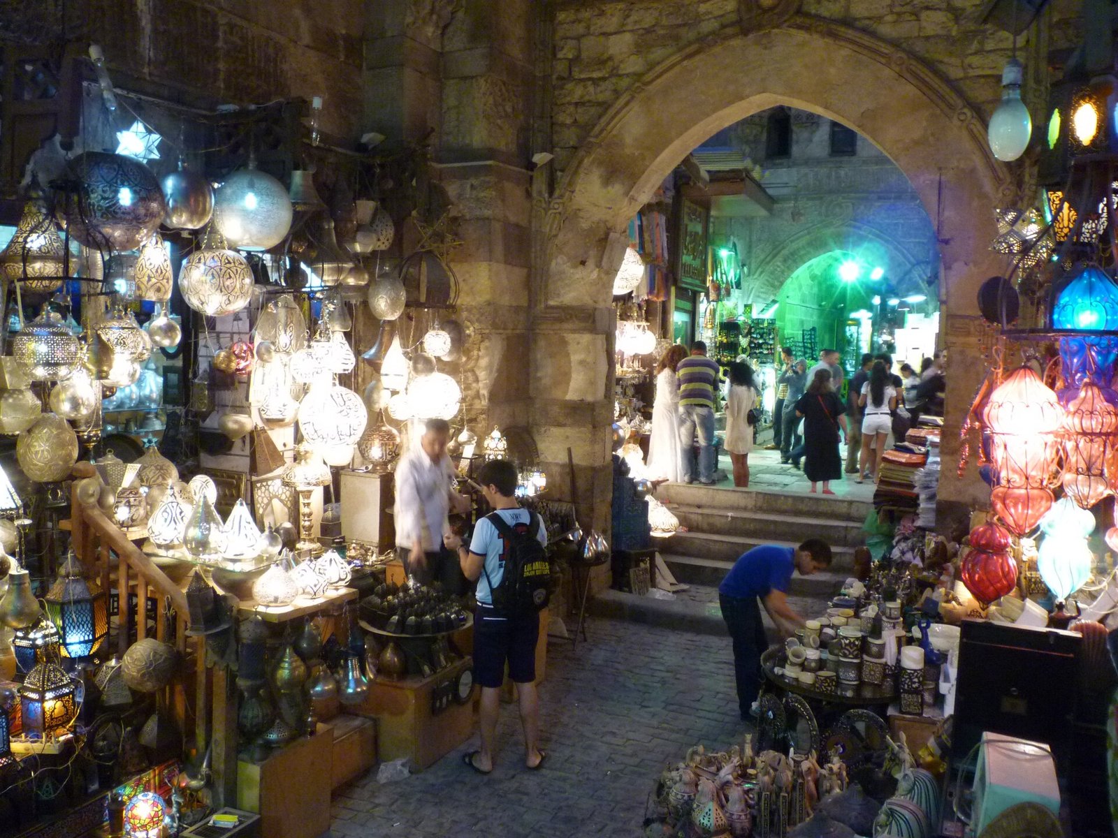 Tienda de lamparas de metal caladas y faroles de colores iluminados bajo arcos de piedra en el bazar Khan el-Khalili de El Cairo con compradores