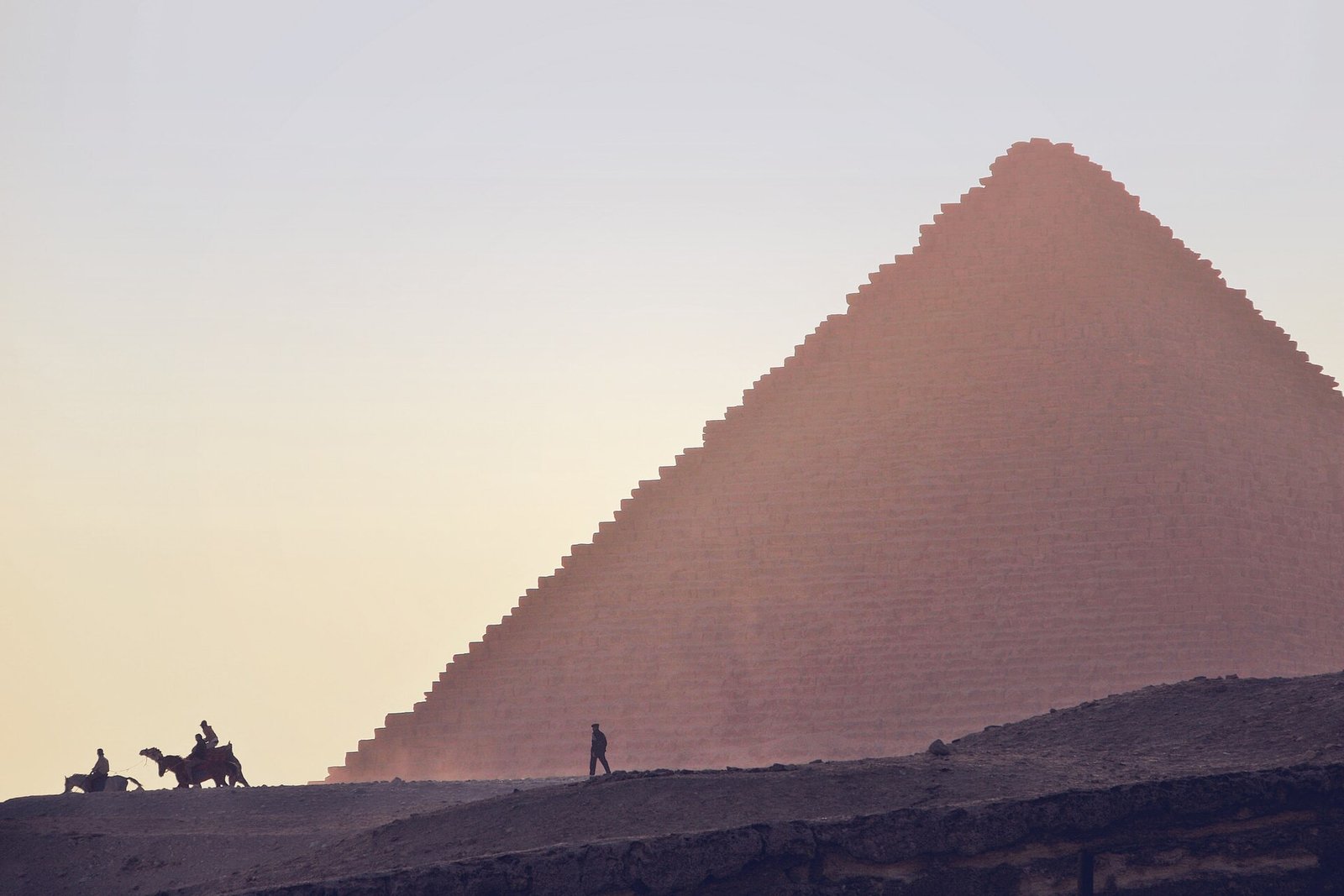 Jinetes en silueta sobre una loma frente a la gran piramide de Giza banada por la luz rosada y dorada del amanecer en Egipto