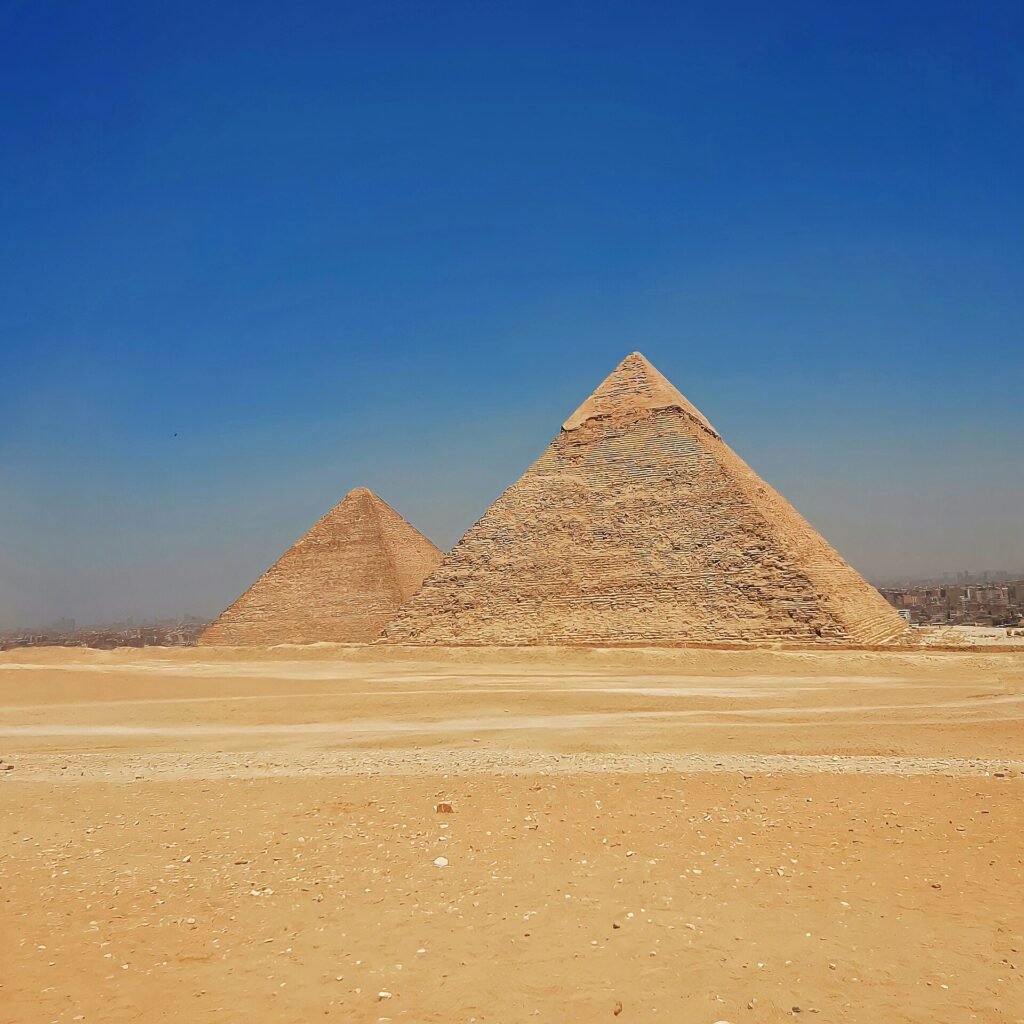 Las piramides de Giza de Kefren y Keops sobre la arena dorada del desierto bajo un cielo azul intenso, mostrando su escala monumental y silueta iconica
