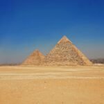 Las piramides de Giza de Kefren y Keops sobre la arena dorada del desierto bajo un cielo azul intenso, mostrando su escala monumental y silueta iconica