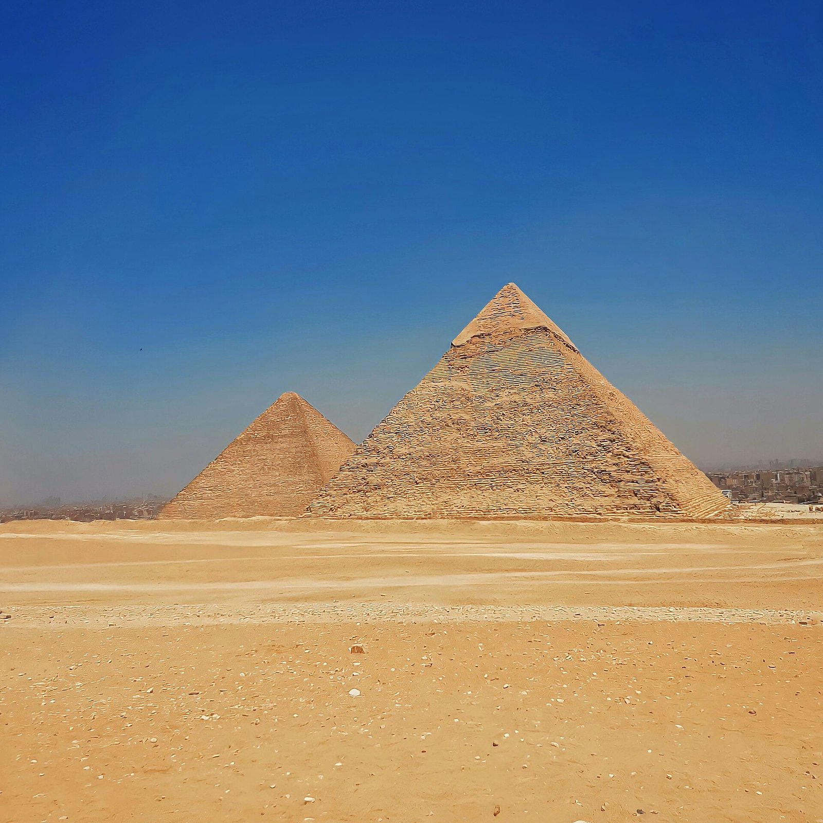 Las piramides de Giza de Kefren y Keops sobre la arena dorada del desierto bajo un cielo azul intenso, mostrando su escala monumental y silueta iconica