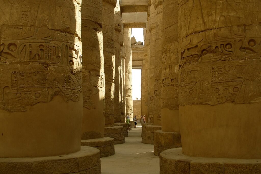 Gran sala hipostila del templo de Karnak en Luxor con columnas doradas talladas con jeroglificos y un viajero al fondo para dar escala
