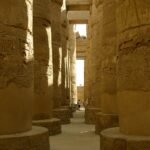 Gran sala hipostila del templo de Karnak en Luxor con columnas doradas talladas con jeroglificos y un viajero al fondo para dar escala