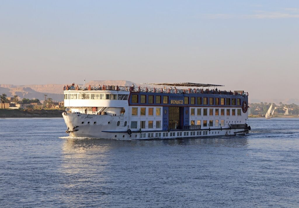 Crucero por el Nilo navegando durante un viaje de 7 dias por Egipto, con vista frontal del barco sobre el rio al atardecer y montanas al fondo