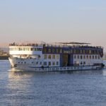 Crucero por el Nilo navegando durante un viaje de 7 dias por Egipto, con vista frontal del barco sobre el rio al atardecer y montanas al fondo