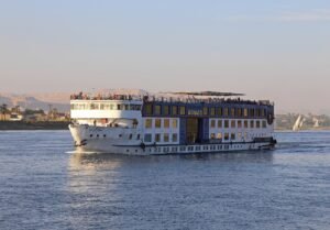 Crucero por el Nilo navegando durante un viaje de 7 dias por Egipto, con vista frontal del barco sobre el rio al atardecer y montanas al fondo