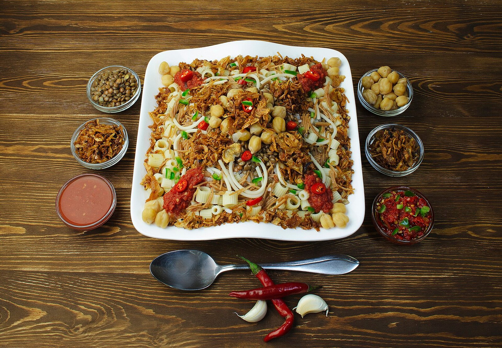 Plato de koshari egipcio con arroz lentejas garbanzos macarrones y cebolla frita servido en mesa de madera comida tradicional de Egipto