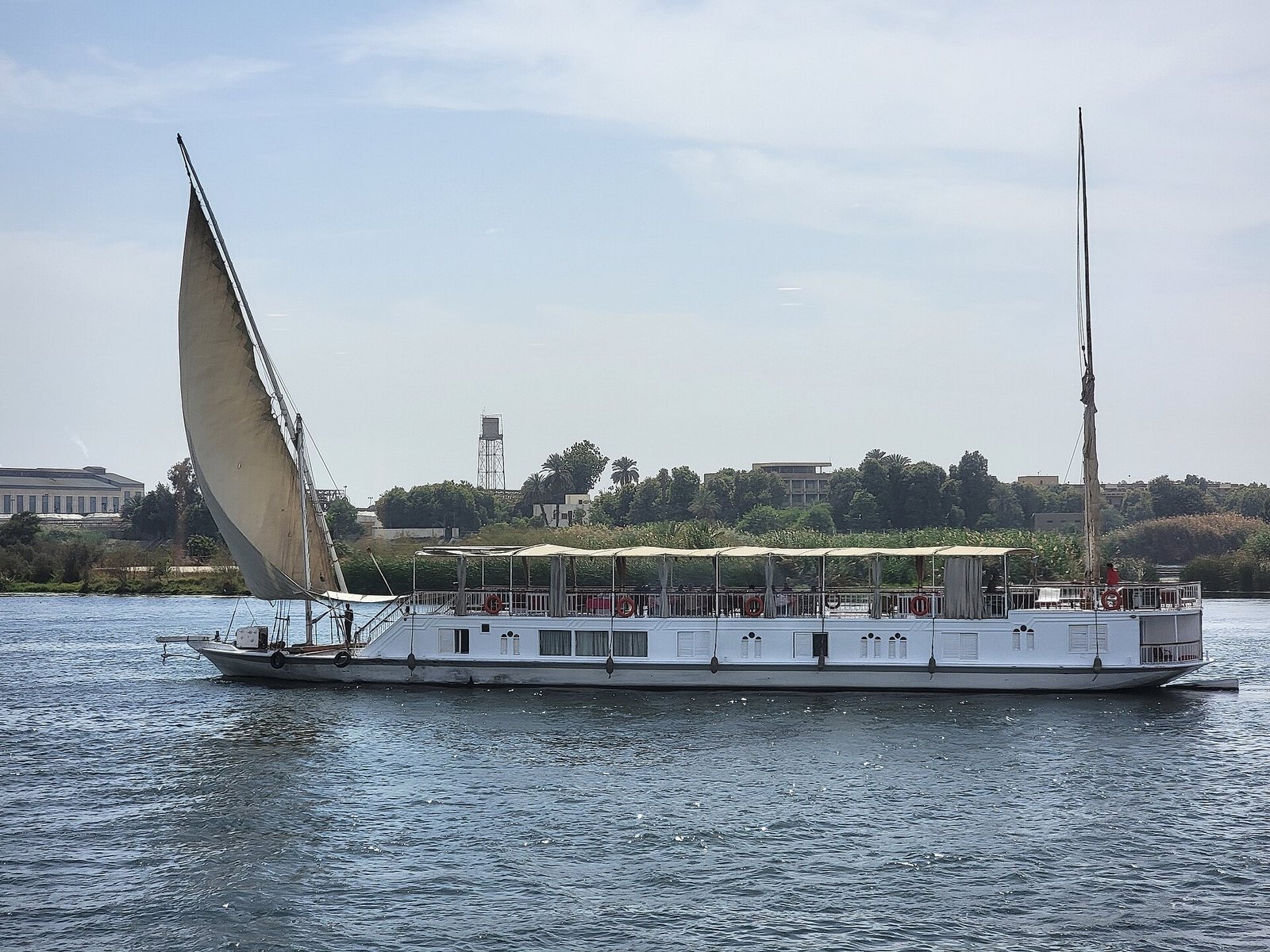 Dahabiya tradicional con gran vela latina blanca desplegada navegando por el Nilo en Egipto
