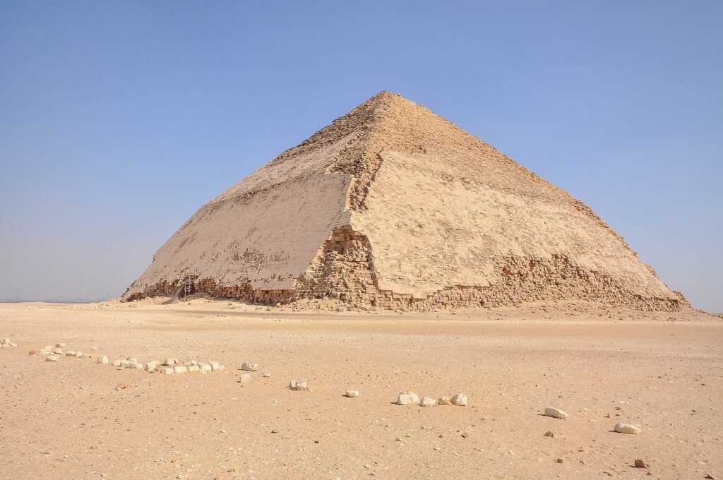 La Piramide Acodada de Dahshur en Egipto mostrando su distintiva doble inclinacion bajo un cielo azul intenso sobre el desierto abierto y dorado