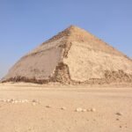 La Piramide Acodada de Dahshur en Egipto mostrando su distintiva doble inclinacion bajo un cielo azul intenso sobre el desierto abierto y dorado