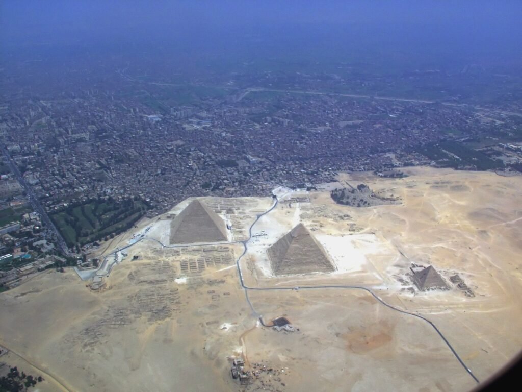 Vista aerea de las tres piramides de Giza sobre la arena dorada con la extensa ciudad de El Cairo al fondo bajo un cielo azul despejado