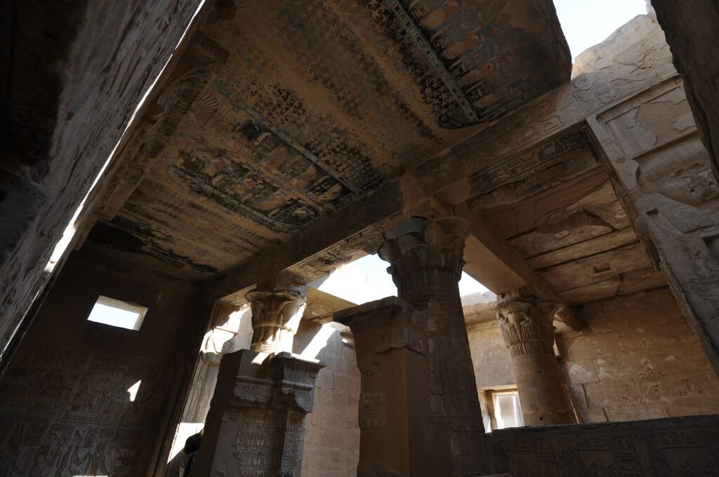 Sala hipostila de un templo ptolemaico bien conservado en Deir el-Medina, Luxor, Egipto, con techo pintado y capiteles tallados iluminados por el sol