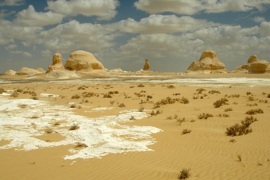 Formaciones de tiza blanca tipo hongo sobre arena dorada ondulada bajo cielo azul con nubes en el Desierto Blanco de Egipto cerca de Farafra