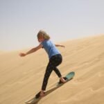 Aventura en el desierto de Egipto, una persona haciendo sandboard descendiendo una gran duna dorada bajo cielo despejado, escena energica y premium