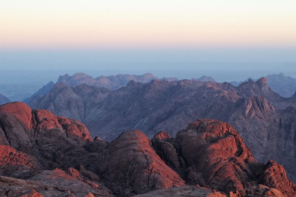 Amanecer sobre las montanas de granito rojo del Monte Sinai en Egipto, con cumbres iluminadas de rosa y dorado y cordilleras azules difuminadas al fondo