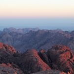 Amanecer sobre las montanas de granito rojo del Monte Sinai en Egipto, con cumbres iluminadas de rosa y dorado y cordilleras azules difuminadas al fondo