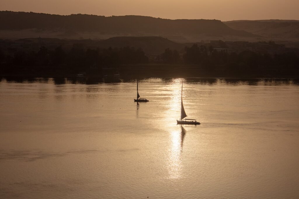 Dos feluccas navegando sobre el Nilo dorado al atardecer con el reflejo del sol en el agua
