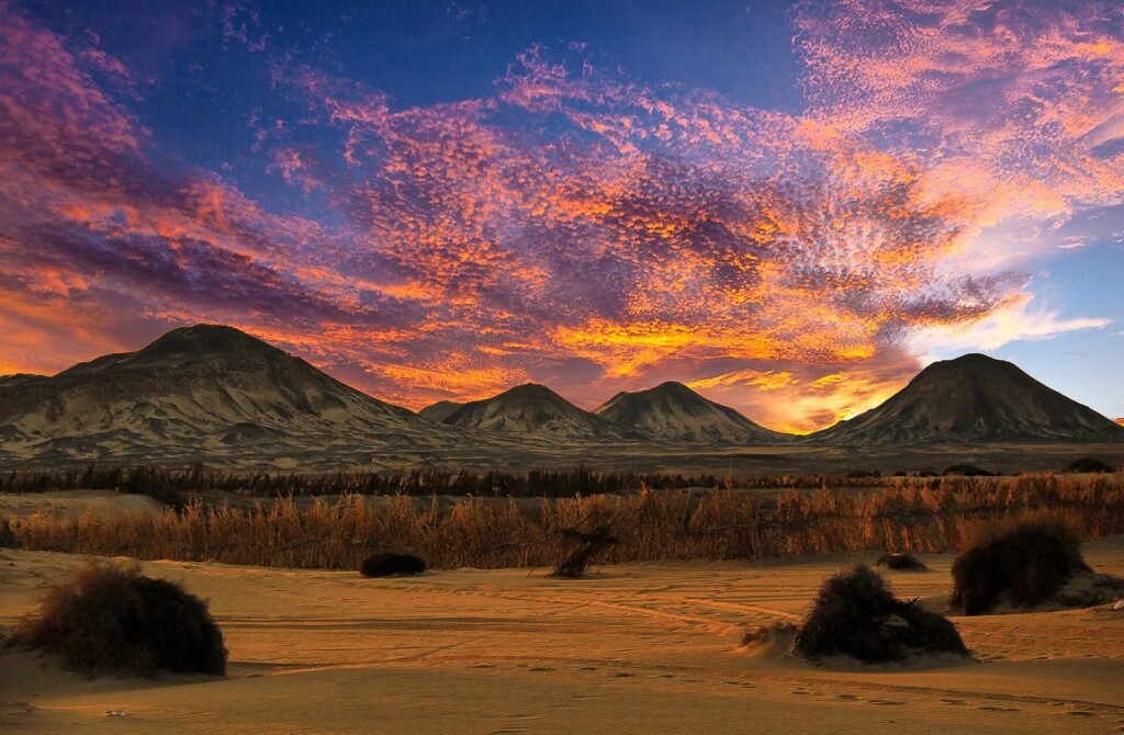 Desierto egipcio al atardecer con nubes rosas y naranjas sobre montanas oscuras y llanuras doradas, paisaje evocador fuera de lo tipico