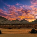 Desierto egipcio al atardecer con nubes rosas y naranjas sobre montanas oscuras y llanuras doradas, paisaje evocador fuera de lo tipico