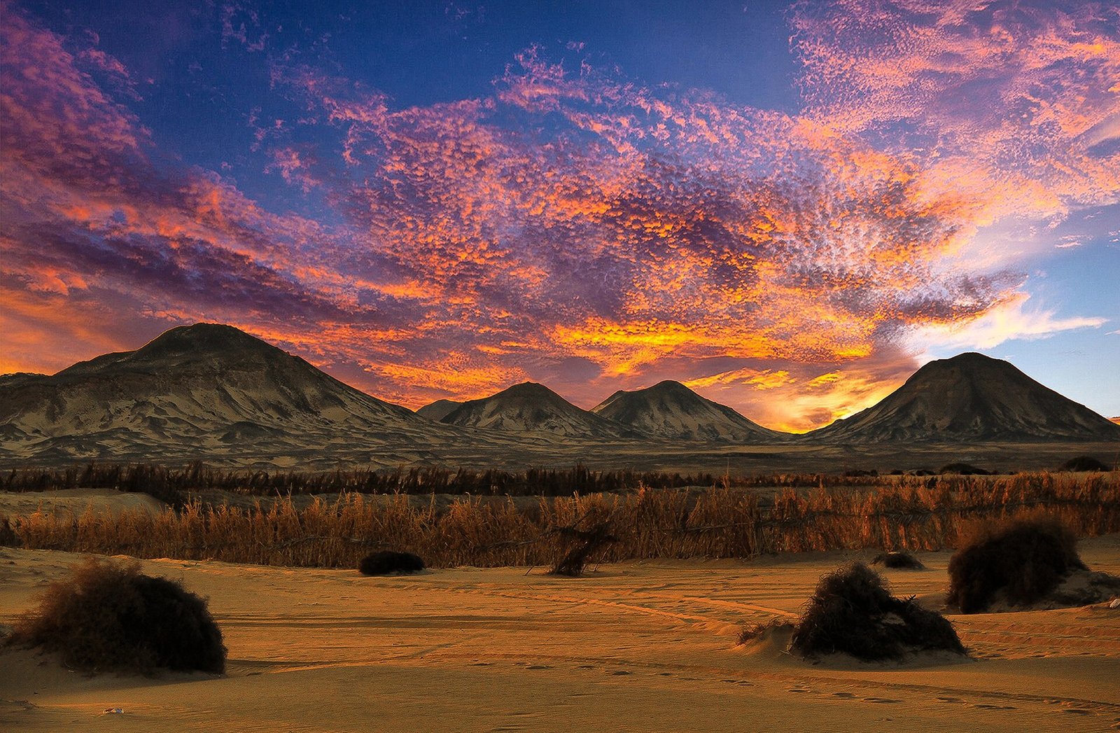 Desierto egipcio al atardecer con nubes rosas y naranjas sobre montanas oscuras y llanuras doradas, paisaje evocador fuera de lo tipico