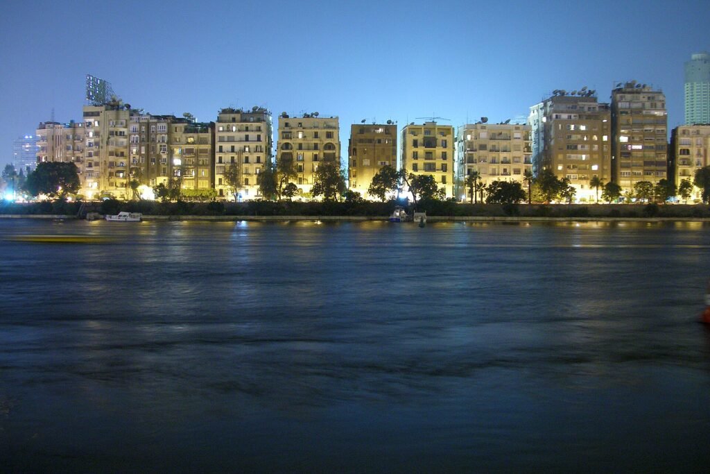 Horizonte de El Cairo al atardecer sobre el rio Nilo en Egipto, con edificios iluminados en luz dorada y el agua tranquila en primer plano
