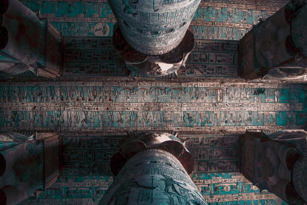 Vista hacia arriba del techo astronomico del templo de Dendera entre dos grandes columnas, con decoracion celeste en tonos turquesa y figuras egipcias