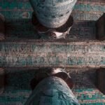Vista hacia arriba del techo astronomico del templo de Dendera entre dos grandes columnas, con decoracion celeste en tonos turquesa y figuras egipcias