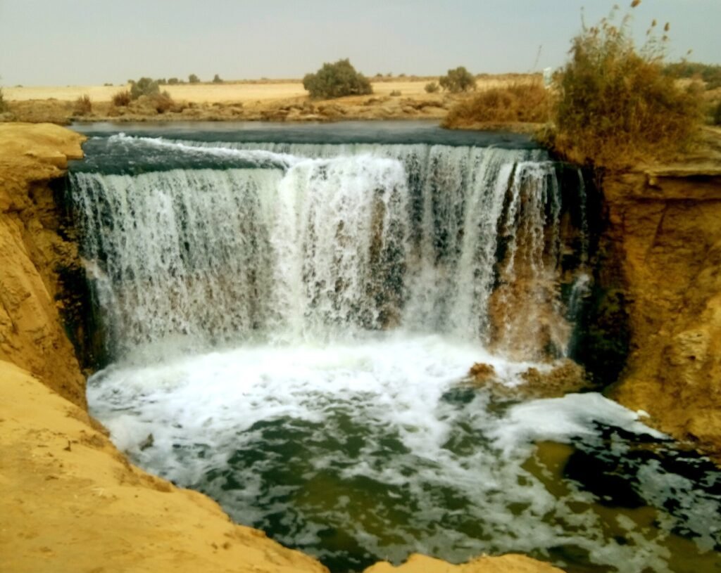 Cascadas de Wadi El Rayan cayendo sobre roca dorada hacia una piscina turquesa rodeada de arena del desierto en el oasis de El Fayum, Egipto