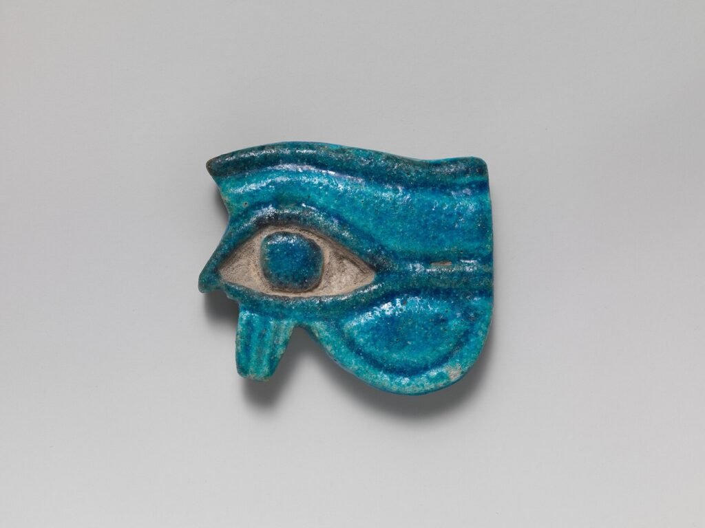 Amuleto wedjat egipcio en fayenza turquesa vidriada, con ceja, ojo y pupila bien definidos, simbolo protector del Ojo de Horus sobre fondo neutro
