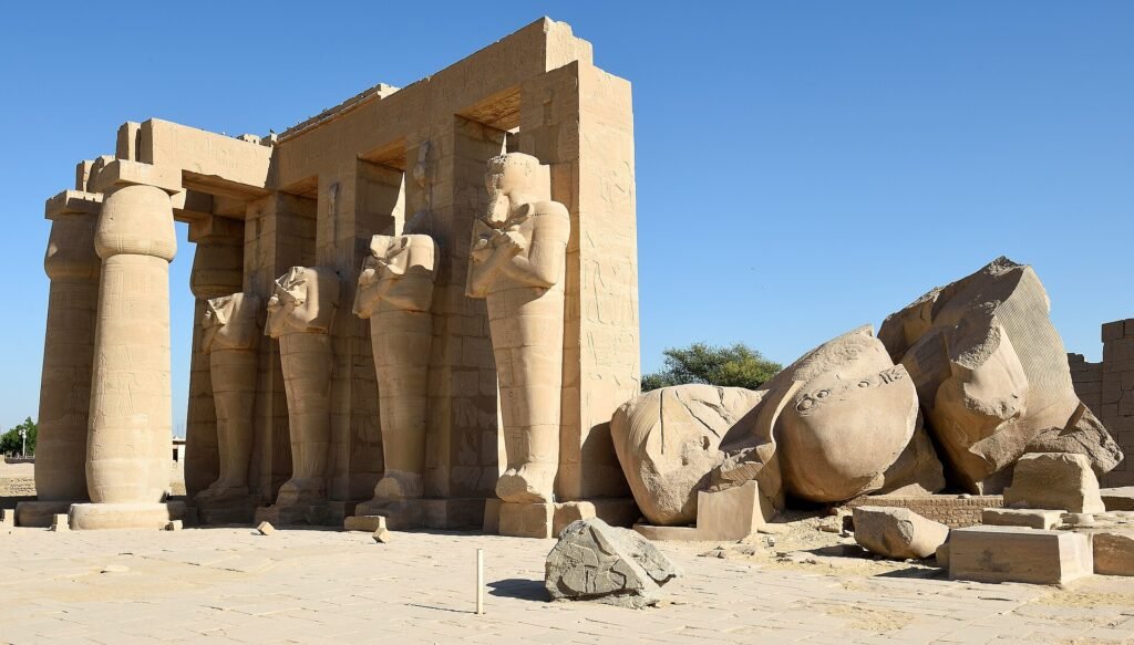 Coloso caído de Ramsés II junto a los pilares osiriacos en pie del templo funerario del Ramesseum en Luxor bajo cielo despejado, Egipto