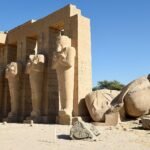 Coloso caído de Ramsés II junto a los pilares osiriacos en pie del templo funerario del Ramesseum en Luxor bajo cielo despejado, Egipto